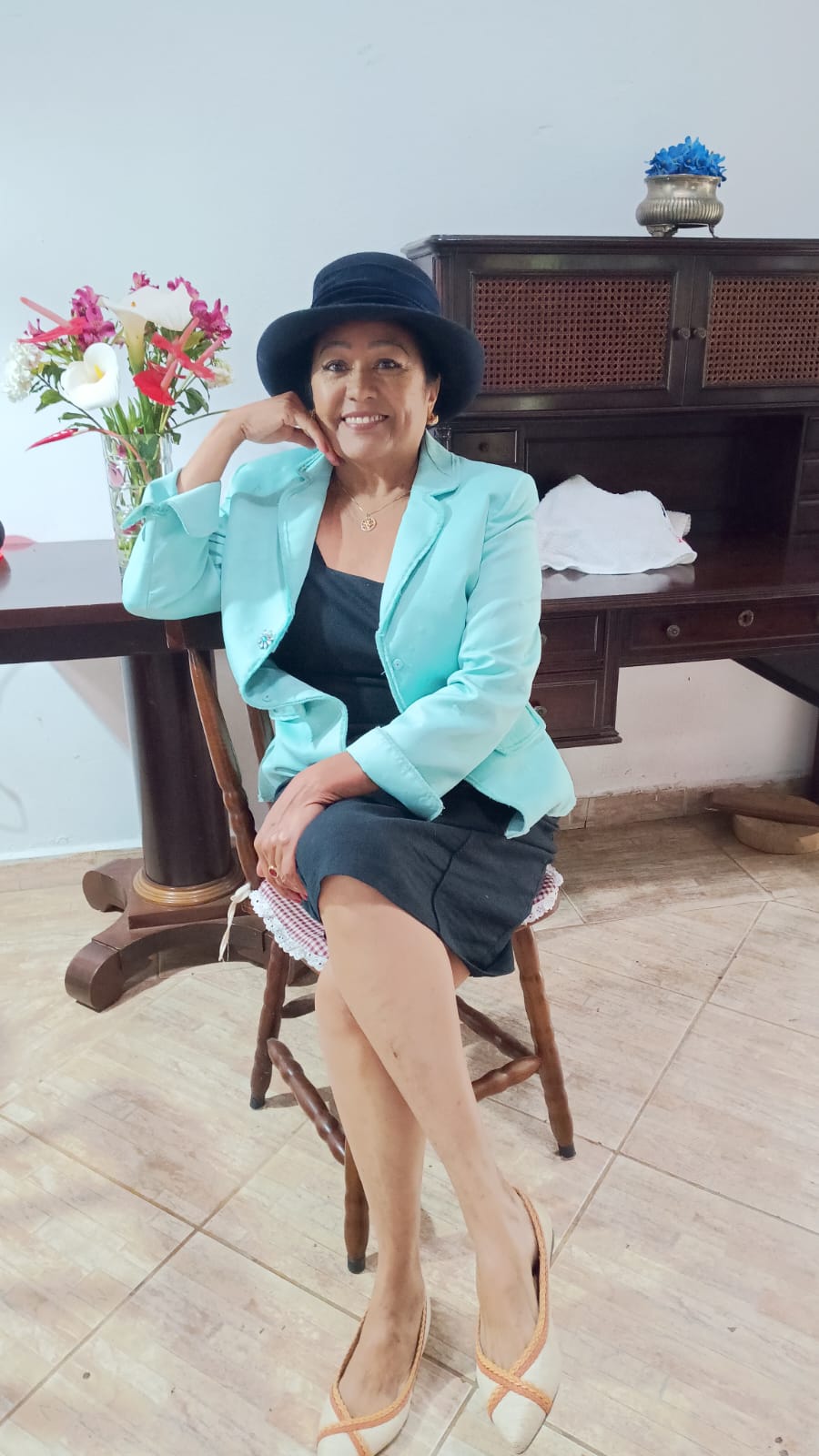 Ana, da Ana Porto Antiguidades, sentada em ambiente com móveis de madeira e flores